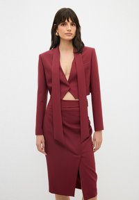 Burgundský přizpůsobený blazer s dlouhými rukávy, hlubokým V-výstřihem a detailem uzlu. Ladící tužková sukně s bočním rozparkem a texturovanou látkou.