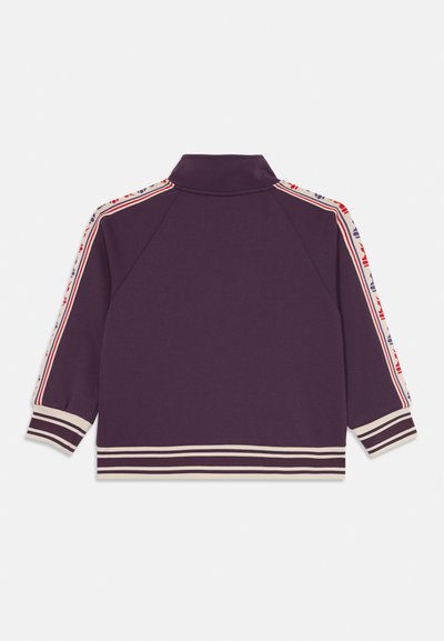Lila Trainingsjacke mit gestreiften Bündchen und Saum, gemusterten weißen, roten und lila Seitestreifen an den Ärmeln und einem Stehkragen, von hinten gezeigt.