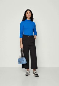 Pulover albastru ajustat cu gât, pantaloni largi negri și o geantă matlasată de un albastru deschis. Adidașii au un amestec de accente negre și argintii.