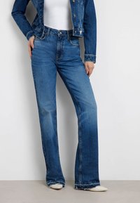 Jeans en denim bleu évasés avec une taille mi-haute, poches avant et finition délavée. Offre des coutures piquées et des ourlets effilochés.