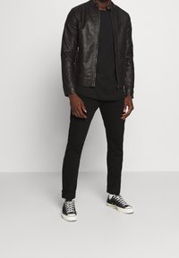 Giubbotto in pelle nera con chiusura a zip, abbinato a una t-shirt nera, jeans neri slim-fit e sneakers nere basse. Outfit semplice e monocromatico.