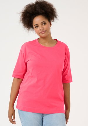 Camiseta de manga corta de color rosa hecha de tejido suave, con un escote redondo y un ajuste holgado, combinada con unos vaqueros de mezclilla azul claro.