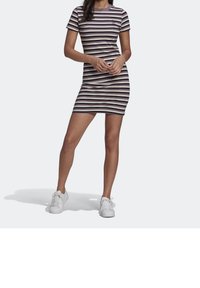 Kvinna som bär en kortärmad klänning i knä-längd med horisontella svarta, lila och vita ränder, i kombination med vita sneakers.