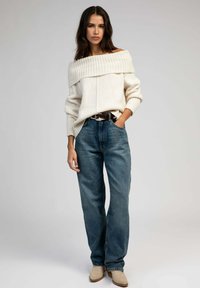 Pull en tricot épais avec un design décolleté, associé à un jean en denim bleu ample et des bottines beiges à la cheville.
