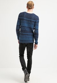 Niebieski i granatowy sweter w paski z okrągłym dekoltem, zestawiony z czarnymi obcisłymi dżinsami i czarnymi skórzanymi butami. Widok od tyłu.