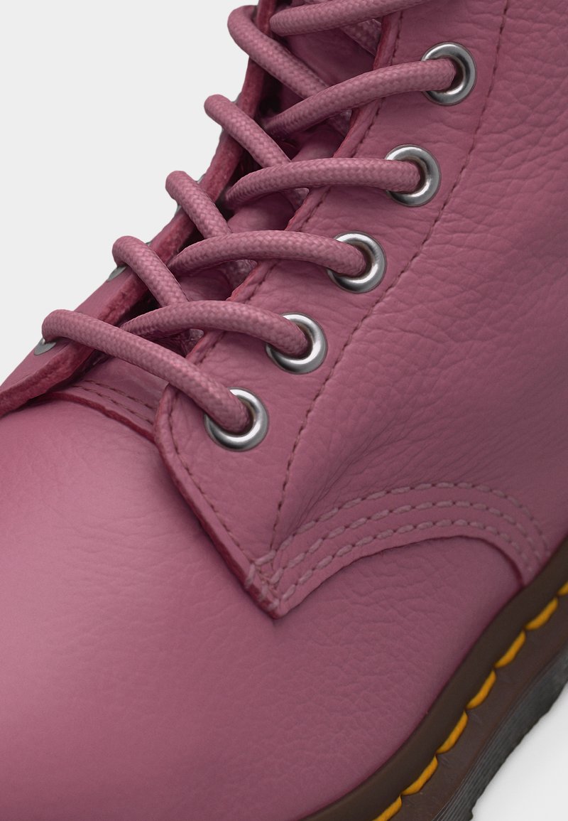 Close-up of pink leather boot with textured surface, silver eyelets, pink laces, visible stitching, and a brown sole with yellow stitching.