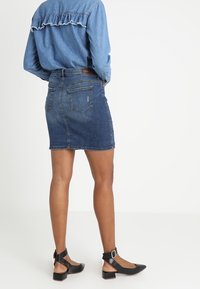 Jupe en denim avec un design ajusté et un ourlet effiloché. Associée à une chemise en chambray bleu avec un empiècement froncé, soulignée par des talons noirs.