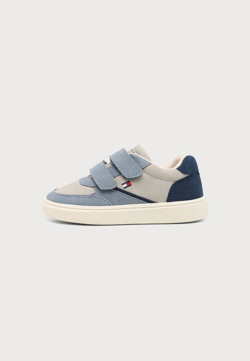 Παιδικό sneaker χαμηλού προφίλ σε ανοιχτό γκρι και μπλε με δύο λουριά με βέλκρο και μικρό λογότυπο με σημαία στο πλάι, σε απλό φόντο.