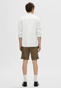 Balta ilgaa rašyto marškiniai su suknežintomis rankovėmis, derinami su rudi šortai ir balti kojinai. Juodi batai baigia aprangą. Vaizdas iš nugaros.