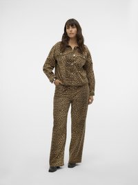Donna in piedi che indossa una giacca coordinata e pantaloni a gamba larga con stampa leopardata marrone e nera, con scarpe nere su sfondo bianco.