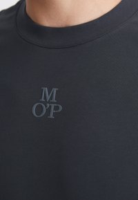 Marinblå kortärmad skjorta gjord av slät tyg med rund hals och präglad logotyp "M O'P" på bröstet i samma färg.