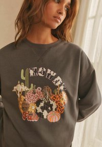 Gray sweatshirt featuring a colorful fall-themed graphic with pumpkins, cacti, and "Howdy" text. Textured material and crew neck design.