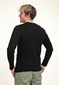 Černé dlouhé rukávy tričko s kulatým výstřihem, vyrobené z hladké, elastické látky. Zadní strana má jednoduchý design bez zdobení.