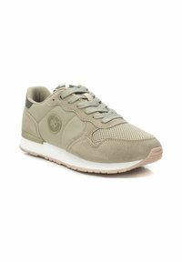 Zapatilla ligera de color beige claro que presenta una combinación de materiales de ante y malla, con cierre de cordones, cuello acolchado y suela de goma blanca.