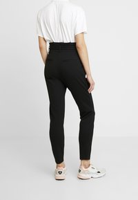 Svarta högmidjade byxor med en figurnära passform, med en mjuk textur och bakfickor, i kombination med ljusrosa och vita sneakers.