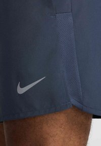 Navyblå atletiska shorts med en slät yta, som har en ventilerande meshpanel och en reflekterande grå Nike-logotyp på den nedre vänstra sidan.