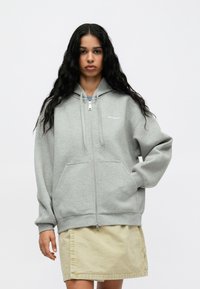 Γκρι φούτερ με φερμουάρ, διαθέτει τσέπη καγκουρό, κουκούλα με κορδόνι και ριμπ μανίκια. Μαλακό ύφασμα με ελάχιστο λογότυπο στο στήθος.