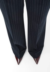Marineblauwe pinstripe broek met een brede pijp en een gestructureerde pasvorm, gecombineerd met puntige bordeauxrode patentleren hakken.