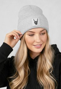 Gray knitted beanie with a ribbed texture and a square white patch featuring a black skeletal hand graphic, snugly fitted.