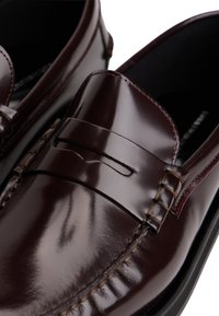 Bordó bőr mokaszinok fényes felülettel, díszített penny szíjjal és részletes varrással a széleken. Látható fekete bélés.