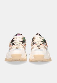 Zapatillas blancas voluminosas con acentos metálicos, detalles de malla y suela de goma beige. Presentan elementos reflectantes y hardware decorativo.