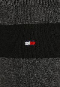 Calze corte grigie con strisce nere. Un piccolo logo con colori rosso, bianco e blu è visibile sul bordo. Materiale a maglia testurizzata.