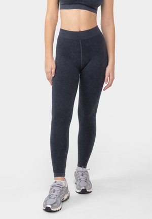Dark grey leggings with a high waistband, a smooth texture, and a fitted shape. Paired with light grey athletic shoes.