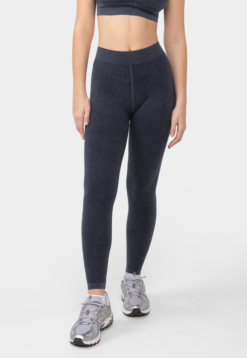 Leggings gris foncé avec une taille haute, une texture lisse et une coupe ajustée. Associés à des chaussures de sport gris clair.