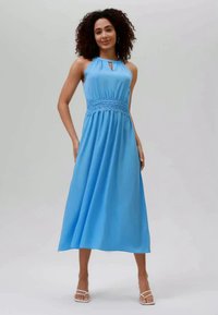 Modré šaty s halter výstřihem, přiléhavým živůtkem a krajkovým detailem v pase. Sukně má hladkou strukturu a sahá do poloviny lýtek.