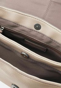 Interno di una borsa in pelle beige con foderatura marrone chiaro, dotata di una tasca con zip e chiusure a scatto metalliche. Sono visibili dettagli in pelle testurizzata.