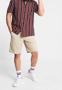 Kortarmige blouse met verticale strepen in rood en marineblauw, gecombineerd met tan knielange shorts en witte sneakers met rode accenten.