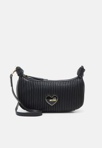 Černá ramenní taška s žebrovanou texturou, zlatým logem ve tvaru srdce a odnímatelným popruhem. Zipové uzavření na vrchu pro snadný přístup.