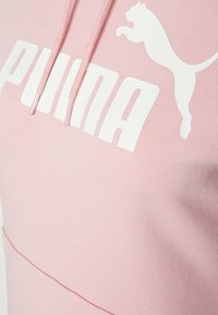Sudadera con capucha rosa hecha de un tejido suave, cuenta con un logotipo blanco de "PUMA" y un gráfico de un puma saltando. Incluye cordones ajustables.