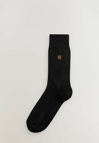 Sort bomuldsstrømpe med en ribbet manchet, der har et lille orange logo på siden. Klassisk design og glat tekstur.