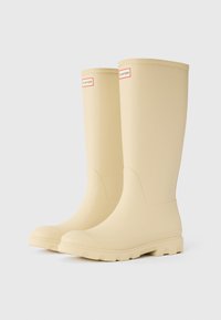Beige rubber knee-high rain boots with textured soles and a smooth finish, featuring a logo patch near the top.