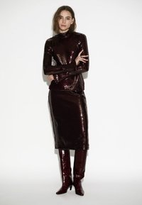 Bordeaux sequined top en rok set met lange mouwen en hoge hals. Glanzende bordeaux kniehoge laarzen. Soepele textuur en strak ontwerp.