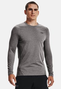 Grå langermet treningsskjorte laget av et teksturert materiale, med rund hals og en liten svart logo på brystet.