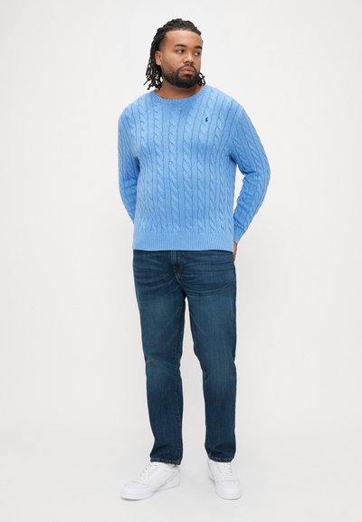 Ανοιχτό μπλε πουλόβερ με πλέξη καλτσών, μακριά μανίκια και στρογγυλή λαιμόκοψη, συνδυασμένο με σκούρο μπλε τζιν και λευκά αθλητικά παπούτσια.