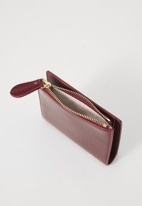 Portafoglio in pelle bordeaux con cerniera dorata, texture liscia, design sottile e un piccolo anello per il fissaggio, aperto leggermente per mostrare l'interno.