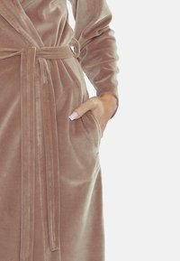 Rochie din catifea de culoare taupe deschis, cu mâneci lungi, talie legată și buzunare laterale. Textură netedă cu un finisaj strălucitor și detalii cusute.