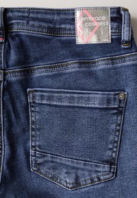 Jeans de mezclilla en azul oscuro con un solo bolsillo trasero, costuras amarillas en contraste y una etiqueta plateada que dice "abraza la comodidad".