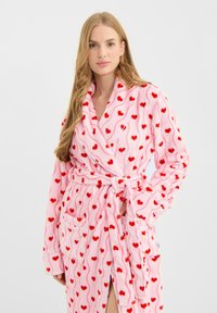 Albornoz de forro polar rosa con un estampado de corazones rojos por todo el tejido, con cuello chal, mangas largas, cinturón para anudar y dos bolsillos delanteros.