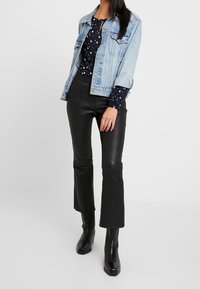 Giacca di denim in lavaggio chiaro, abbinata a un top blu marina con motivi a stelle bianche, pantaloni in pelle neri a zampa d'elefante e stivaletti neri.