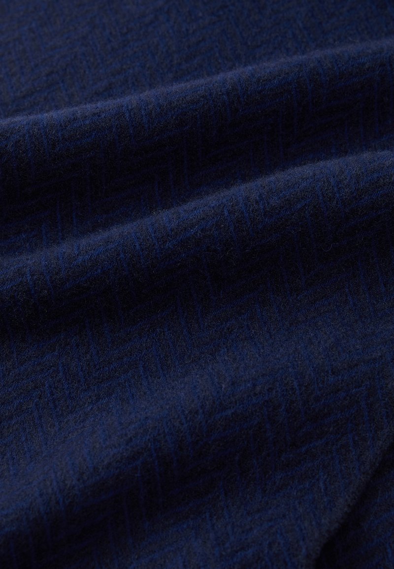 Tissu en laine marine avec un motif en chevrons texturé. La surface semble douce et légèrement duveteuse, avec des plis drapés créant de la profondeur.