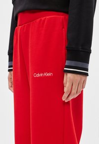 Czerwone dresy z miękkiego materiału z bocznymi kieszeniami, z haftowanym logo Calvin Klein. Połączone z czarną bluzką z długim rękawem.