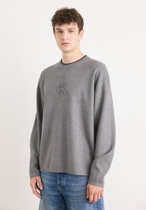 Grijze sweatshirt met een ronde hals, voorzien van een subtiel geborduurd 'CK' logo. Gecombineerd met lichtblauwe denim jeans. Zachte textuur, ontspannen pasvorm.