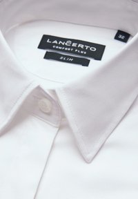 Biała koszula z kołnierzykiem i guzikiem. Metka informuje "LANCERTO COMFORT PLUS SLIM" oraz rozmiar "32". Tkanina wydaje się gładka z delikatnym połyskiem.