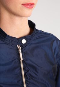 Navy blue lightweight jacket with a textured finish, featuring a stand collar, silver zipper, and snap closure detail.