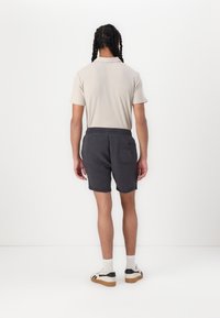 Lys beige polo skjorte med korte ærmer og ribbet tekstur, parret med mørkeblå shorts med elastisk talje og en lomme bagpå.