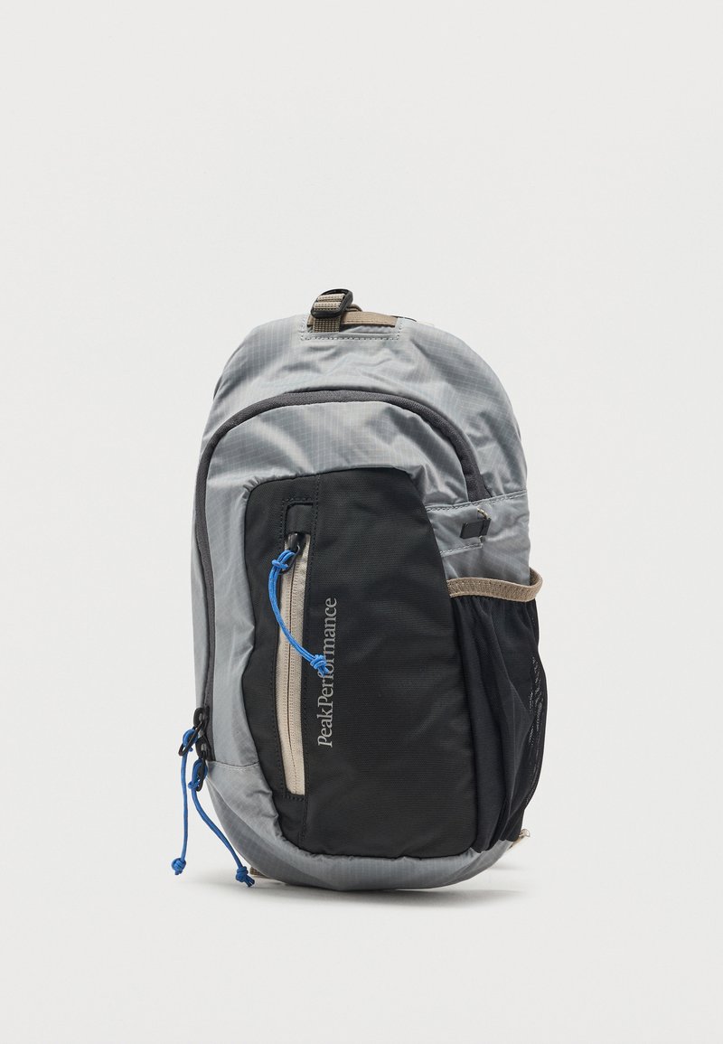 Γκρι και μαύρο συμπαγές σακίδιο πλάτης Peak Performance με φερμουάρ μπροστινή τσέπη, μπλε κορδόνια και δίχτυ πλαϊνή θήκη.